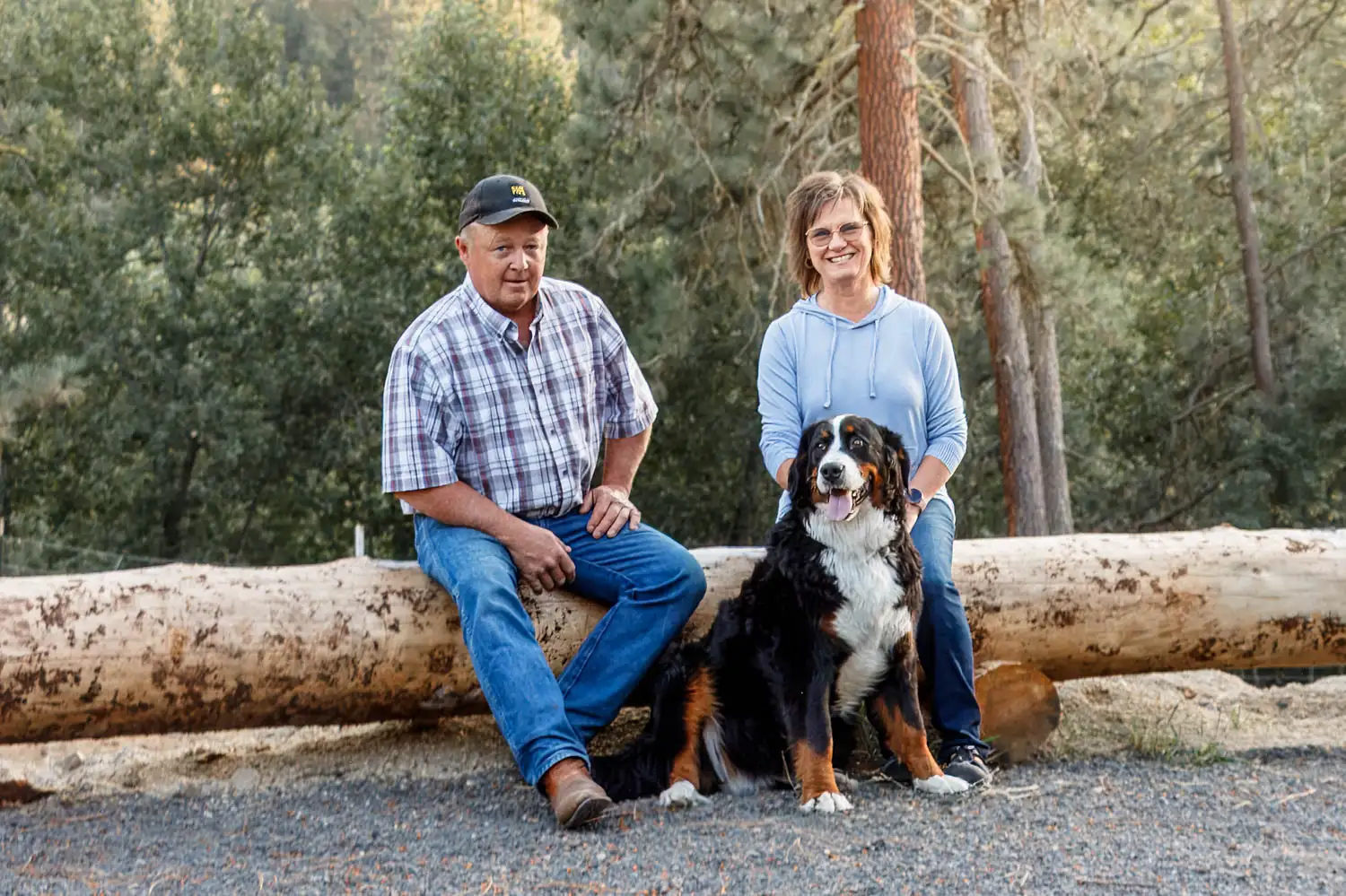 Rodger and Lori Warner sitting with dog outside on a log